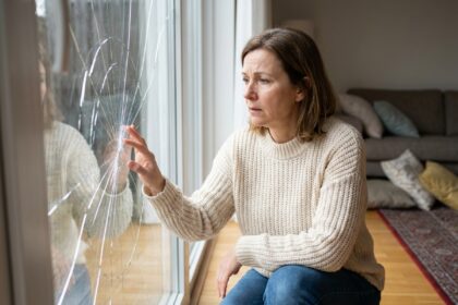 Femme en pull regardant une vitre cassée dans un salon moderne
